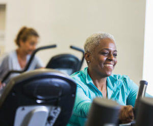 Happy senior African American woman (60s) riding exercise bike, smiling. what is cardiopulmonary rehabilitation