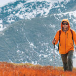 Dressed bright orange jacket backpacker walking by red blueberry