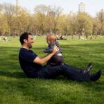 Man holds baby while sitting up in park