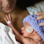 Tiny newborn in purple knit beanie held by mother