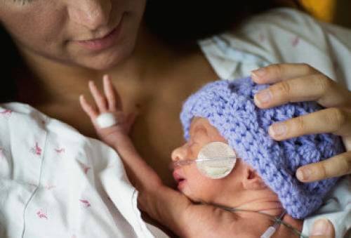 Tiny newborn in purple knit beanie held by mother