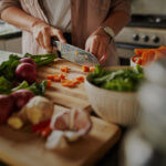 Closeup of young female hands chopping fresh vegetables on chopping board while in modern kitchen