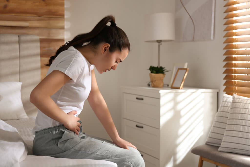 Young woman struggling with stomach ache on bed at home