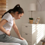 Young woman struggling with stomach ache on bed at home