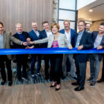 group cutting large blue ribbon at ceremony