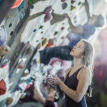 athlete chalking her hands at rock wall of gym