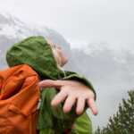 young woman hiker splaying arms out on top of mountain