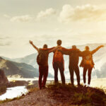 Four happy friends are looking on mountains and having fun together - Four happy friends are looking on mountains and having fun together - Our Connection to People and Place featured image