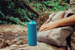Hiker sitting with backpack and bottle of water on nature - how to prevent heat exhaustion image