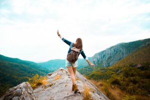 a woman balancing on a rock formation with her hands out as she's hiking - embracing women's health 20s image