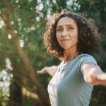 A woman in a green tee shirt doing yoga outdoors - embracing women's health featured image