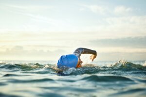 a woman swimming in the ocean wearing a blue swim cap - embracing women's health senior image
