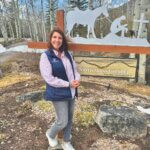 Marion Garrett smiling in front of Snowmass Chapel sign