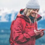 A portrait of a young female nature lover wandering in the mountains, using her mobile phone