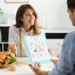 Young nutritionist consulting patient at table in clinic - how a dietitian can help you with your health goals featured image