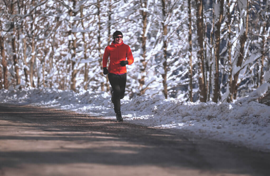 happy motivated smiling sporty 45 years old endurance sport athlete woman running jogging along asphalt road on cold sunny winters day with snow and snowcovered trees following heartfelt advice