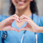 Happy woman, doctor and heart shape hands for love in healthcare or life insurance at the hospital. Female person or medical professional showing hand loving emoji, symbol or sign gesture at clinic.