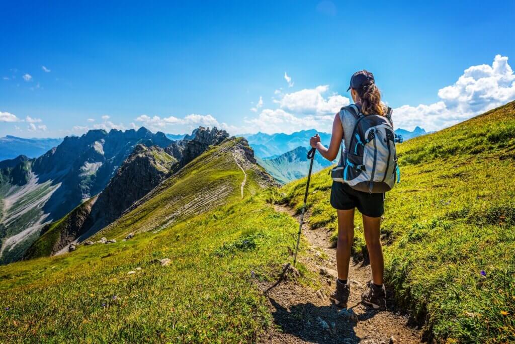 Hiker in boots and backpack holds walking stick as she pauses on dirt mountain pass guide to hiking injuries featured image