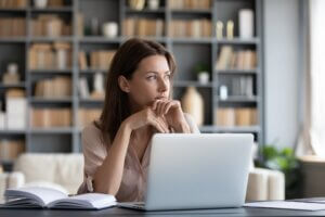 Pensive millennial girl sit at desk look in window distance thinking or dreaming visualizing, thoughtful young woman distracted from computer work pondering over problem solution, lost in thoughts