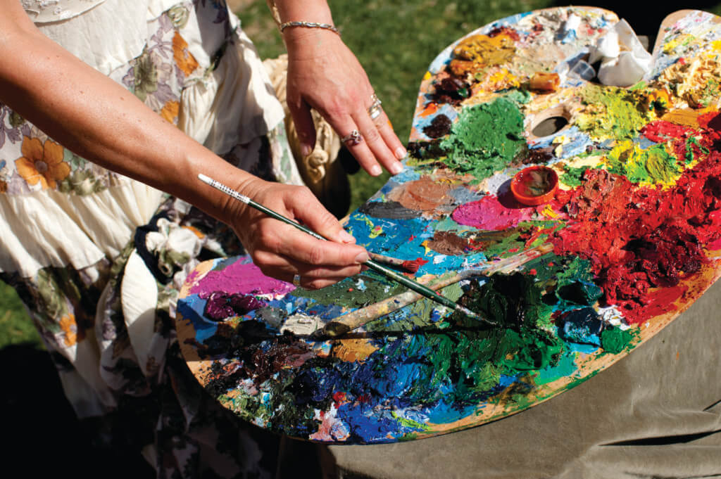 hands drawing paint off of a colorful palette