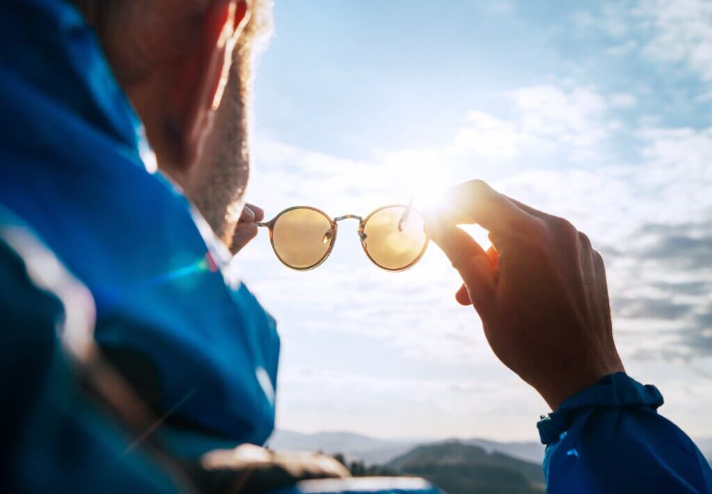 Backpacker man looking at bright sun through polarized sunglasses enjoying mountain landscape. eyes healthy at altitude featured image