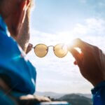 Backpacker man looking at bright sun through polarized sunglasses enjoying mountain landscape. eyes healthy at altitude featured image