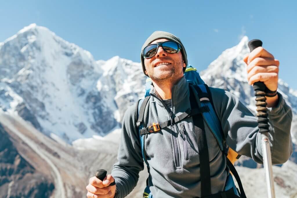 Portrait of smiling Hiker man on Taboche 6495m and Cholatse 6440m peaks background with trekking poles, UV protecting sunglasses. He enjoying mountain views during Everest Base Camp trekking route. proper eye care in the mountains