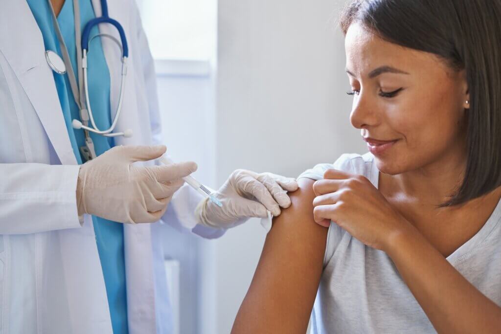 Young happy woman patient receiving injection of vaccine in clinic