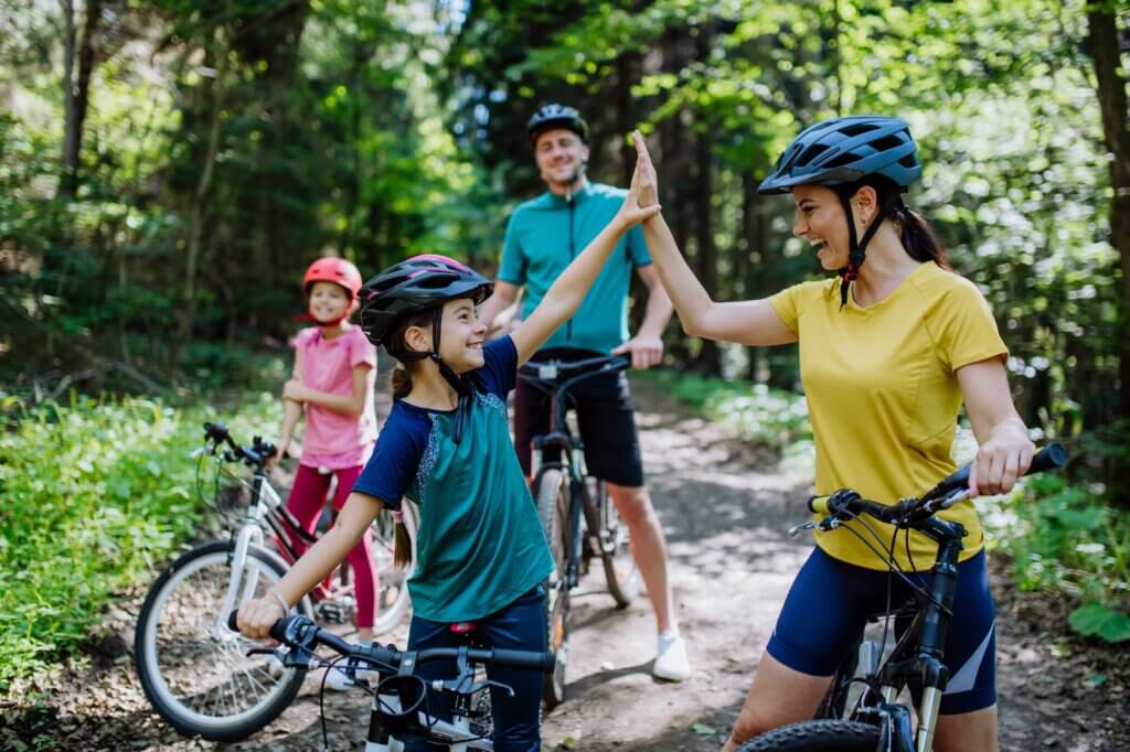 A young family with little children preapring for bike ride, standing with bicycles in nature and high fiving.