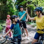 A young family with little children preapring for bike ride, standing with bicycles in nature and high fiving.