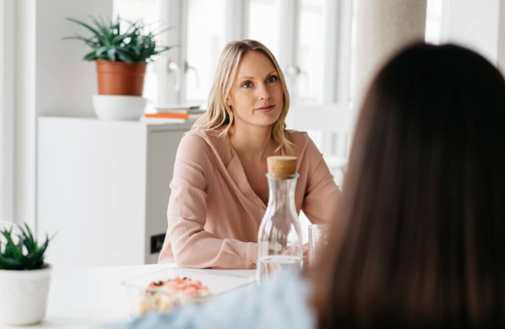 Two office colleagues having a meeting or discussion over refreshments at a cafeteria or canteen in an over the shoulder view of an attentive young woman listening