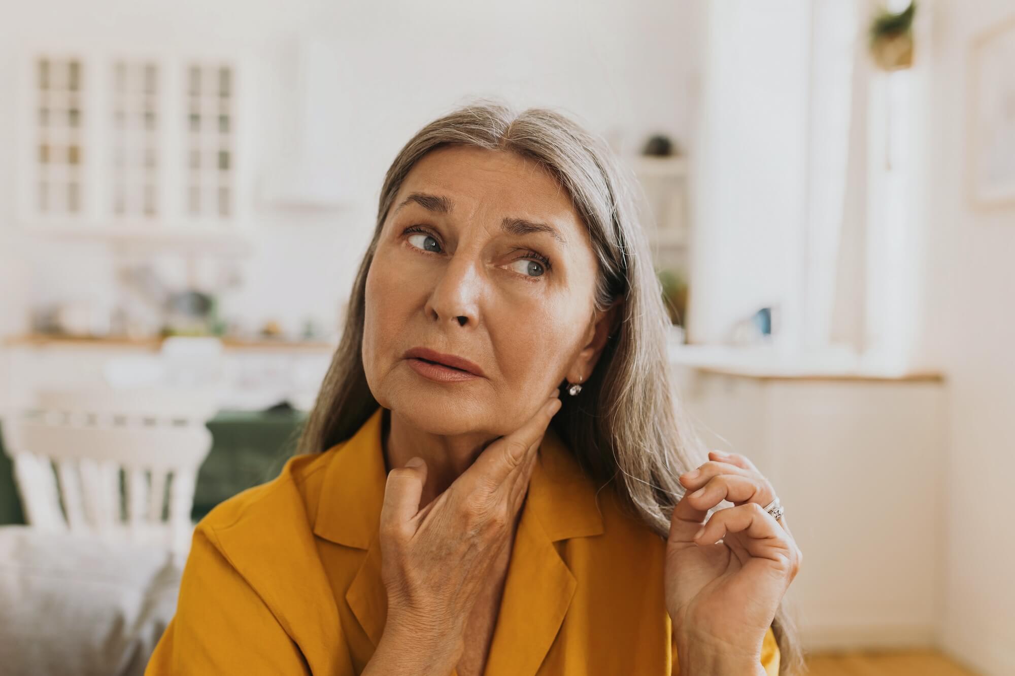 Elderly woman feeling pain, swollen thyroid or lymph nodes.