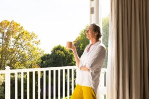 Enjoying morning coffee, mature woman standing on balcony and relaxing self care daily routine