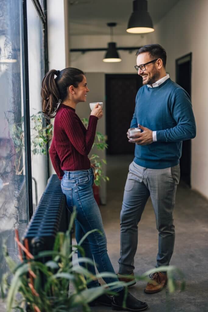 Woman and man, standing in the company hallway, drinking a coffee.