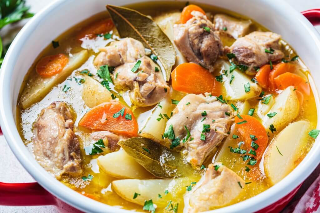 Chicken stew with potatoes and carrots in red pot, close-up. Chicken soup with vegetables and herbs. Comfort food recipe. healthy meals holiday leftovers