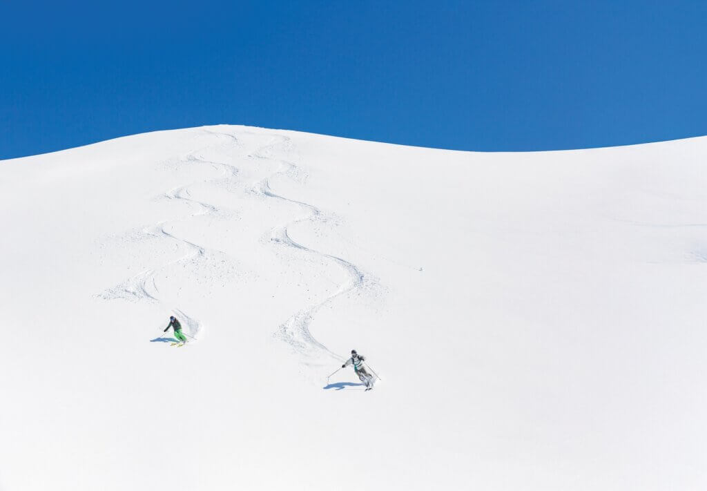 Man and woman skiing down mountain leaving tracks behind