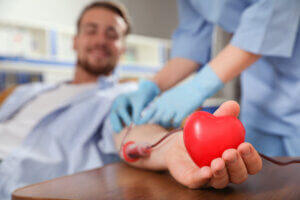 Young man making blood donation in hospital, focus on hand