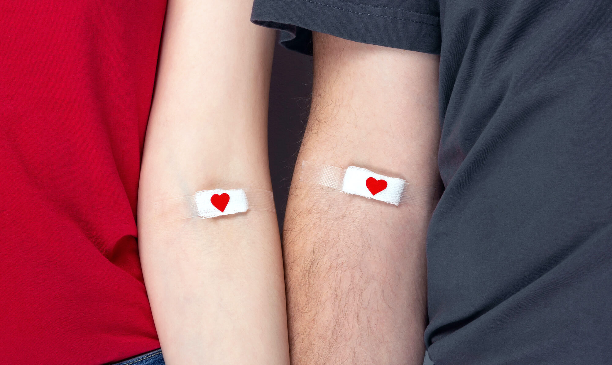 Blood donorship. Man in grey and woman in red T-shirt with hands taped patch after giving blood with red heart