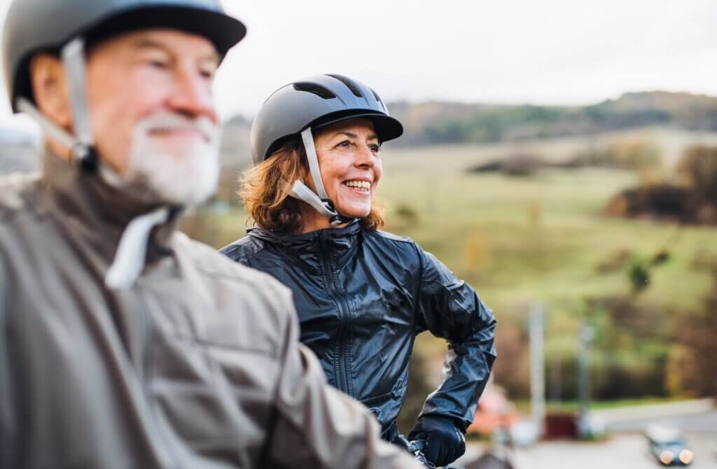 An active senior couple with helmets and electrobikes standing outdoors on a road in nature. lifestyle choices for healthy heart
