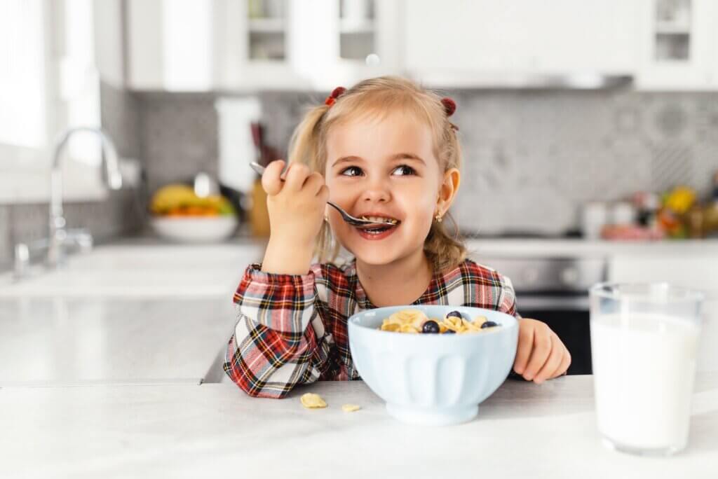 Beautiful little girl having breakfast with cereal, milk and blueberry in kitchen healthy dinner ideas picky eater