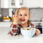 Beautiful little girl having breakfast with cereal, milk and blueberry in kitchen healthy dinner ideas picky eater