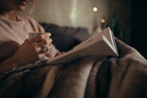 Cropped shot of female hands with book and coffee. Female reading book on bed at night. sleep Hygiene Tips