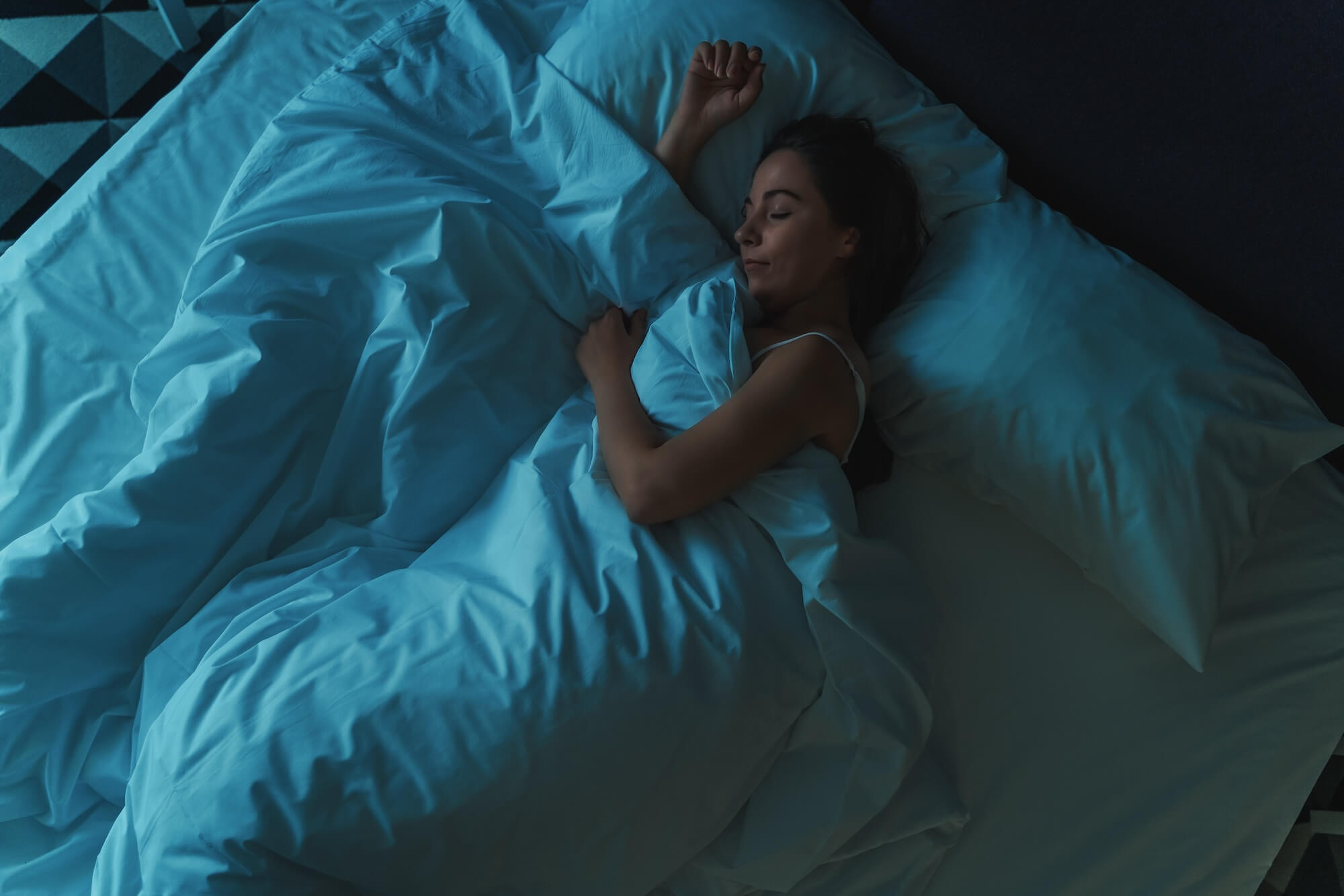 woman sleeping alone in big bed at night, top view, blue toned. sleep hygiene tips