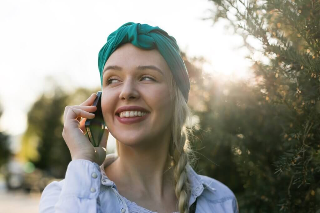 Pretty young Caucasian woman with backpack speaking on the phone outdoors in park laughing. Cute teenage girl with checkered shirt and long blonde hair talking on smart phone. No retouch.