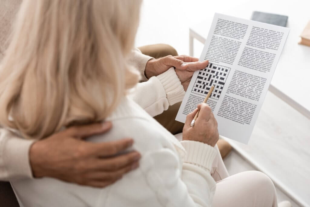 cropped view of senior man hugging wife with pencil and crossword