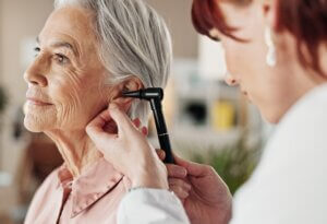 Senior, woman and doctor with otoscope in clinic for ear screening, wellness exam and audio check. Ent, otolaryngology or medical professional with elderly person in hospital for checkup or infection.