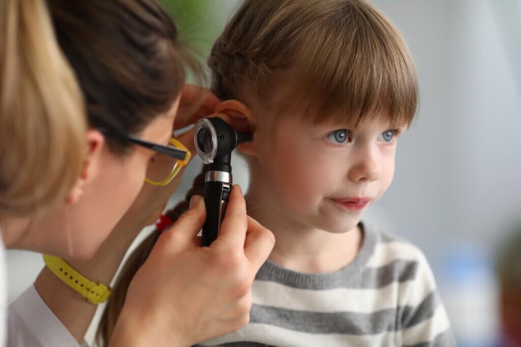 Pediatrician examines ear of sick child in office of hospital background. Otitis Prevention Concept