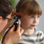 Pediatrician examines ear of sick child in office of hospital background. Otitis Prevention Concept