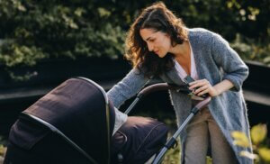 Woman with her baby in stroller outdoors. Mother with baby in pram in neighbourhood.