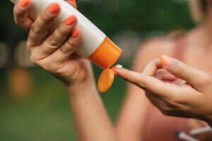 Close-up image of a woman putting on sun lotion, focus on a sun screen and her hand.